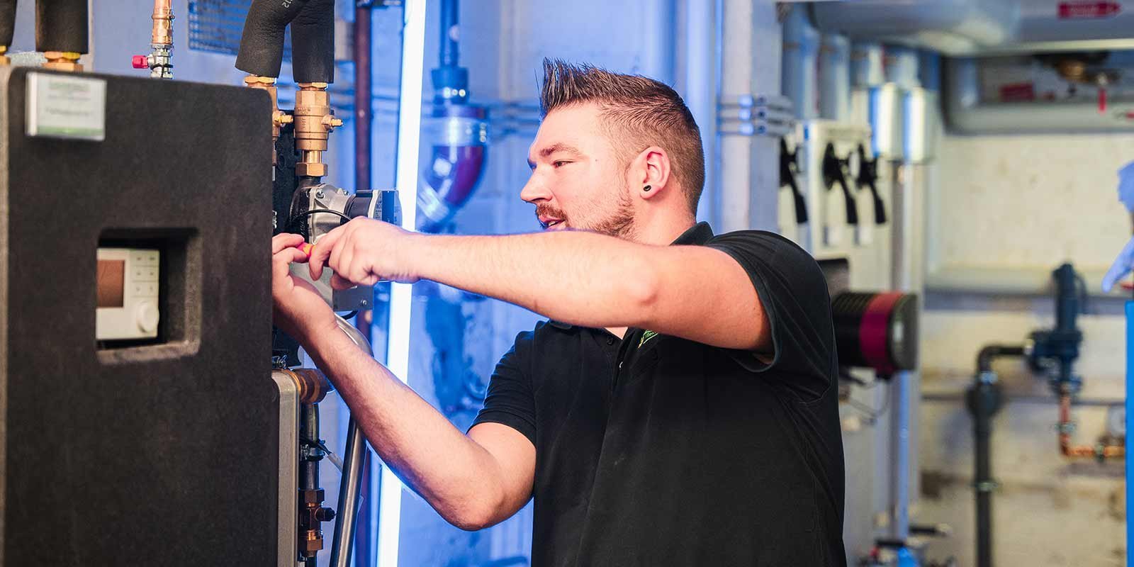 Ein Techniker arbeitet konzentriert an einer Heizungsanlage, während er ein Werkzeug in der Hand hält.