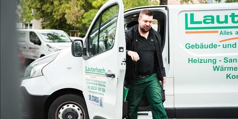 Ein Handwerker steigt aus einem weißen Lieferwagen mit dem Logo 'Lauterbach' und trägt grüne Arbeitskleidung.