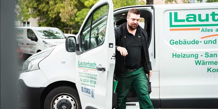 Ein Handwerker steigt aus einem weißen Lieferwagen mit dem Logo 'Lauterbach' und trägt grüne Arbeitskleidung.