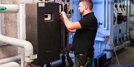 Ein Techniker arbeitet an einer Heizungsanlage, um Rohre und Ventile in einem gut beleuchteten Raum zu überprüfen.