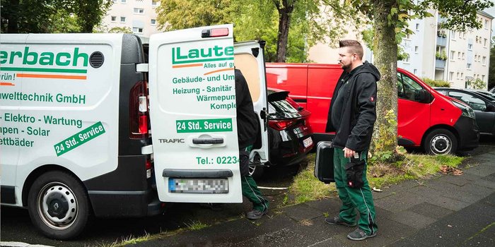 Ein Techniker steht neben einem Lieferwagen, während er eine Werkzeugkiste in der Hand hält und auf die Straße schaut.